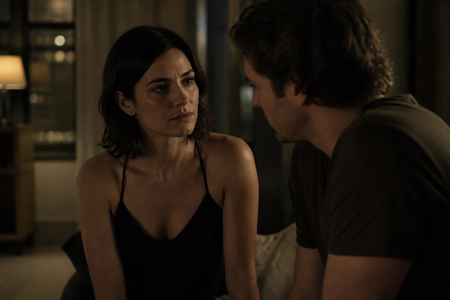 A TV drama still of two characters in a tense night conversation in a dim apartment.
